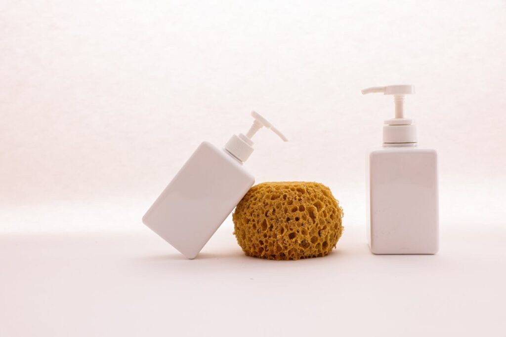 Stylish display of white cosmetic pump bottles and a yellow sponge on a clean white background, embodying minimalist bathroom aesthetics.